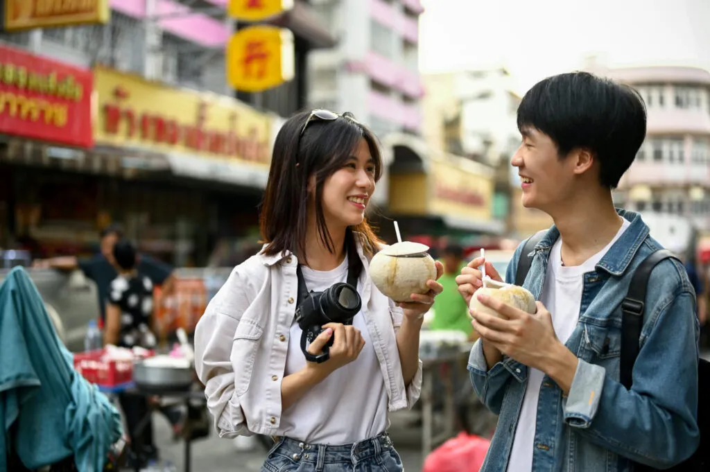 Happy young Asian tourist couple enjoying their fresh coconut drink while sightseeing
